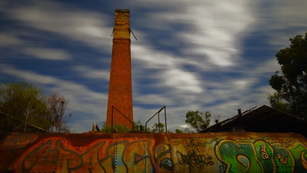 Abandoned smokestack with graffiti and cloudy skies.