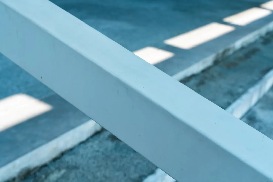 A white railing casts shadows on concrete.